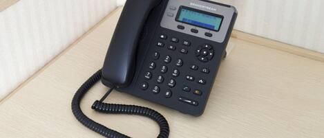 A black telephone with a keypad and a small screen, placed on a wooden surface.
