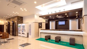 Zona de recepción de un hotel con mostrador de mármol, máquinas expendedoras y una pantalla digital.