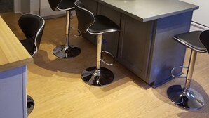 A modern kitchen with white cabinets, a built-in microwave, a sink, and a stove. There are three black bar stools around the island. - Relax Inn this Knotty & Nice entire Home (Evansville)