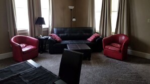 A living room with a black sofa, two red armchairs, a small table, and a lamp. - Relax Inn this Knotty & Nice entire Home (Evansville)