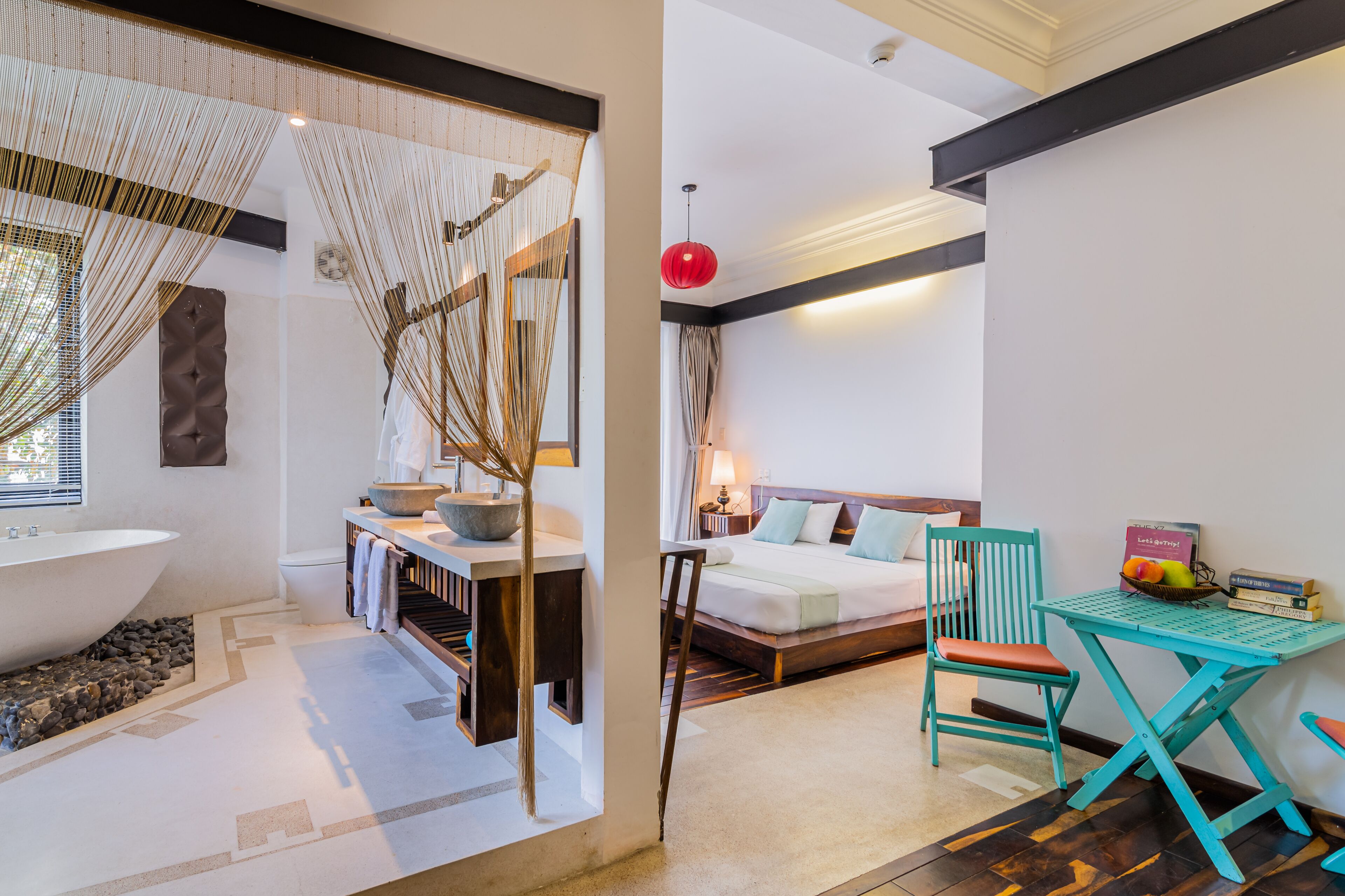 A modern bedroom with a large bed, a desk with a chair, a small table, and a bathtub.