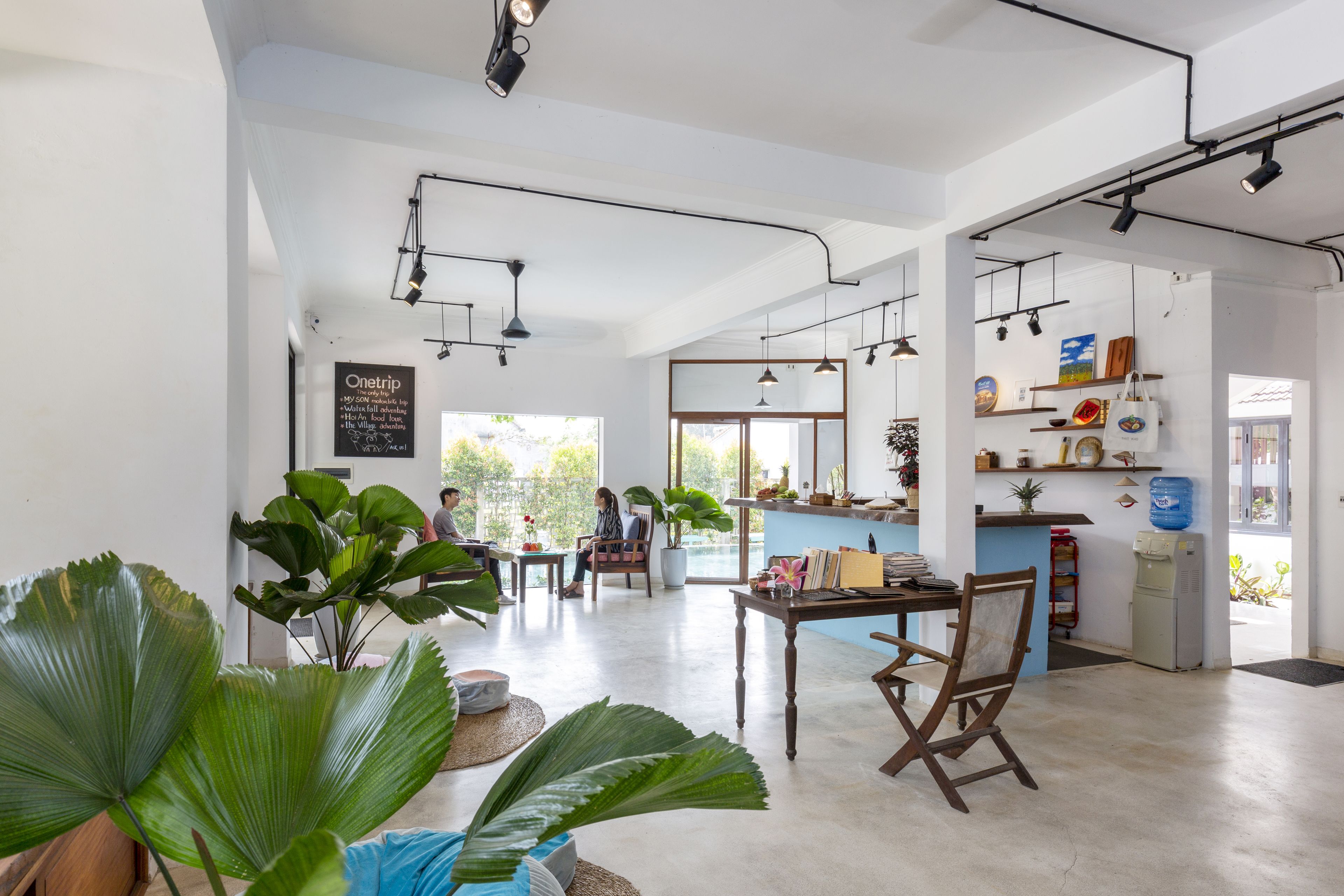 A spacious, well-lit café with large windows, a central table, and seating areas.