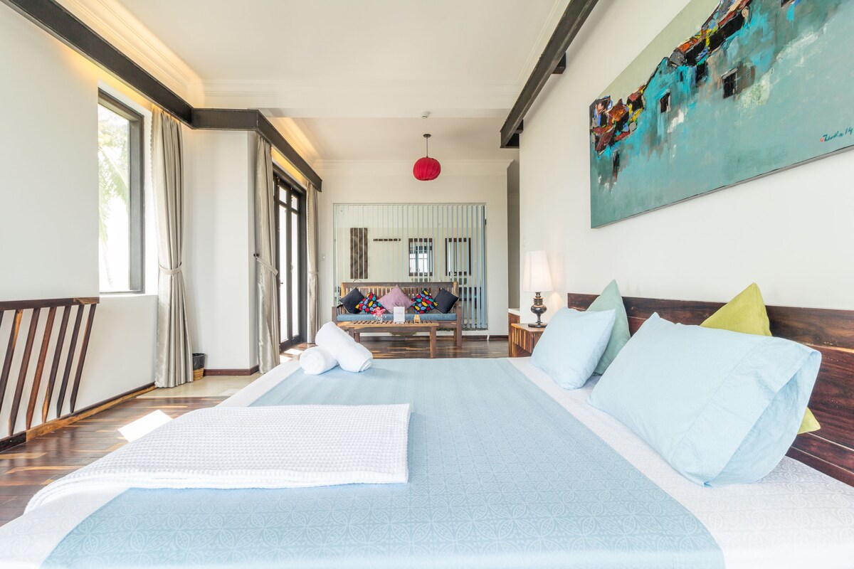 A spacious bedroom with a large bed, a wooden headboard, a painting on the wall, and a view of the balcony.