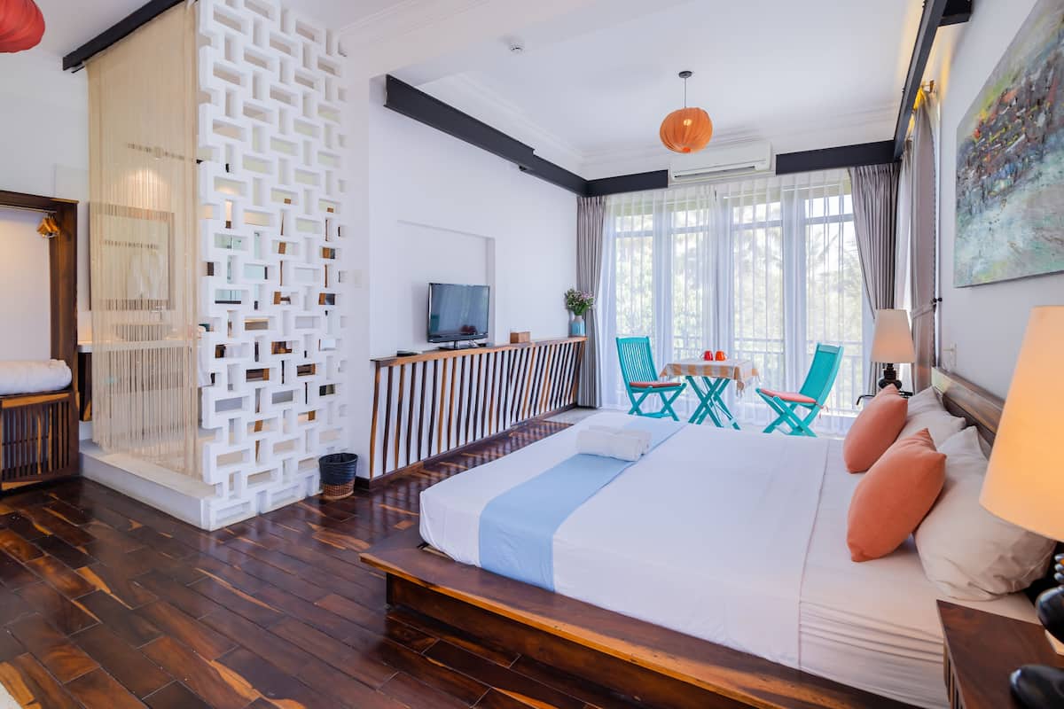 A modern hotel room with a large bed, a TV, a dining area, and a view of the outdoors.