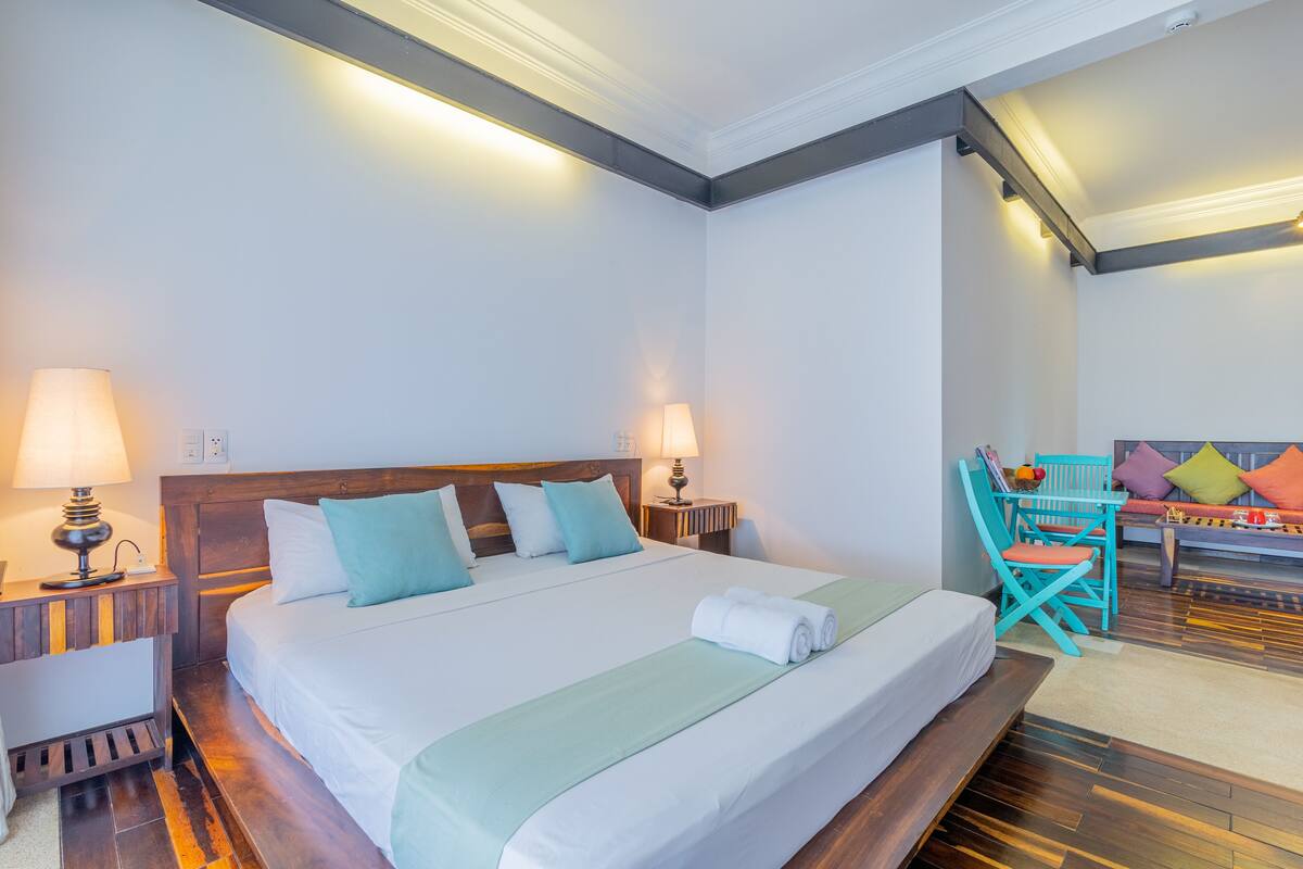 A neatly made bed with a green blanket, two bedside lamps, and a wooden nightstand.