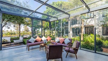 A spacious glass-enclosed patio with modern furniture and lush greenery visible through the glass.