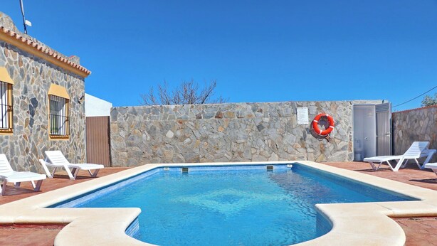 A swimming pool with white lounge chairs and a stone wall. - Perfect house for families with pool (CONIL DE LA FRONTERA)