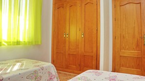 A bedroom with two single beds, a wooden wardrobe, and a window with yellow curtains. - Perfect house for families with pool (CONIL DE LA FRONTERA)