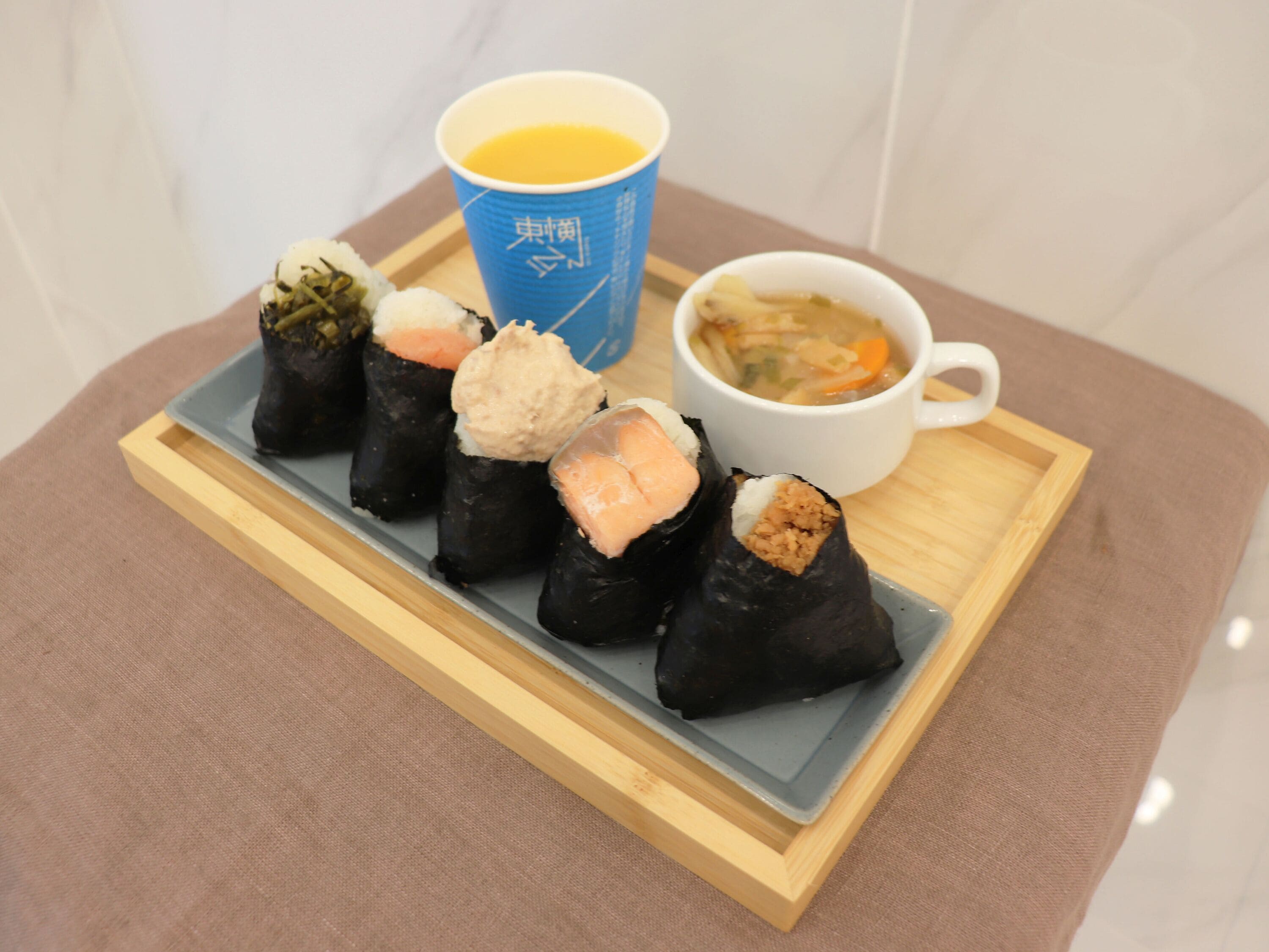 A tray with sushi and a soup cup on a wooden board.