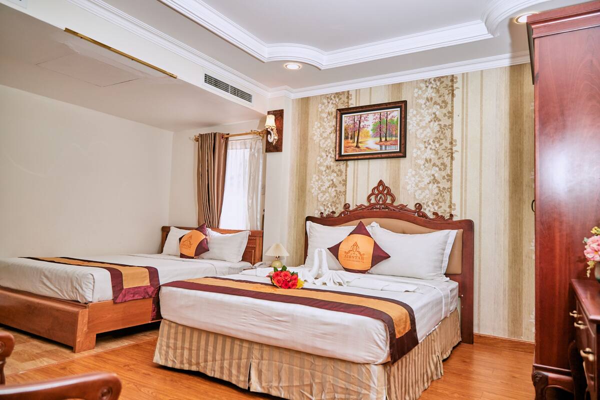 A hotel room with two single beds, a wooden headboard, a painting on the wall, and a wooden cabinet.