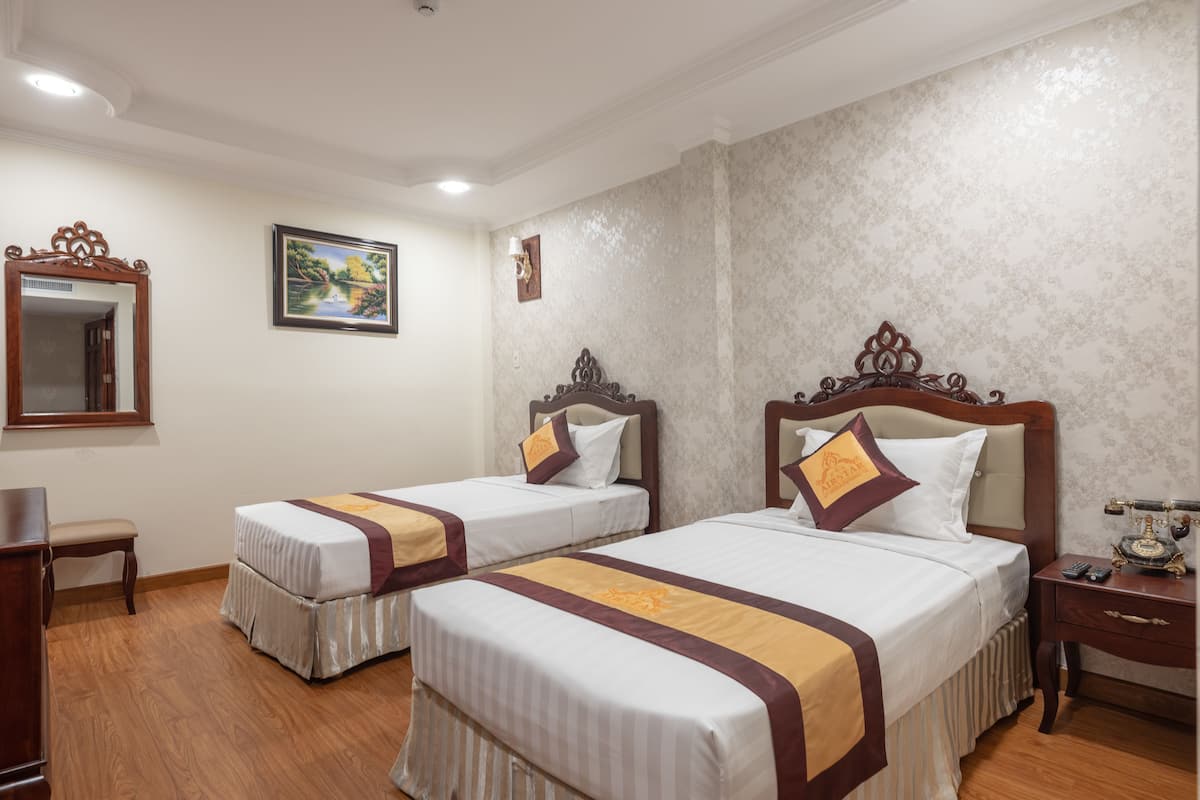 A hotel room with two beds, a wooden floor, a mirror, a framed picture, and a nightstand with a telephone.