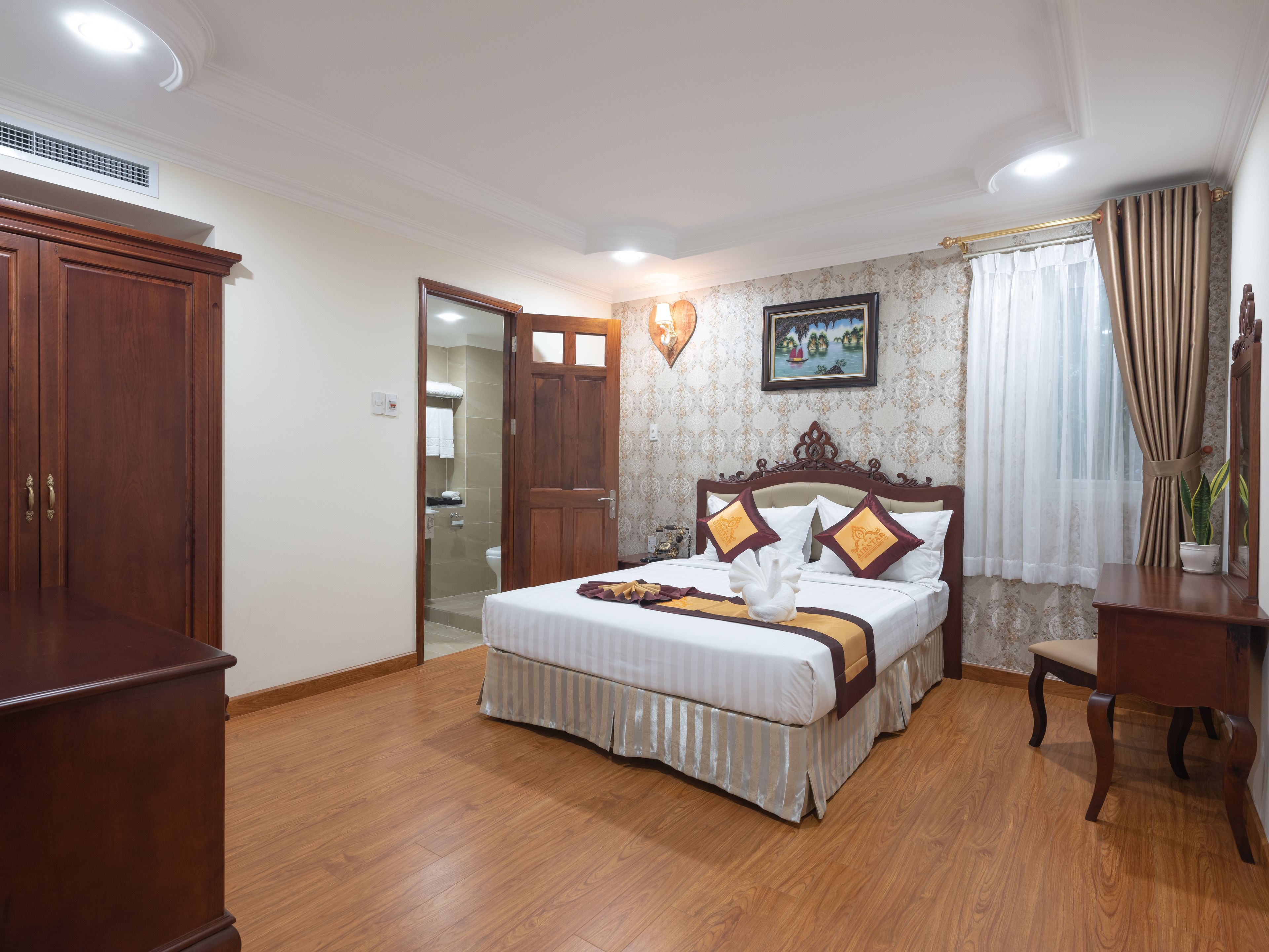 Une chambre à coucher avec un grand lit, une armoire en bois et une salle de bain visible à travers une porte ouverte.