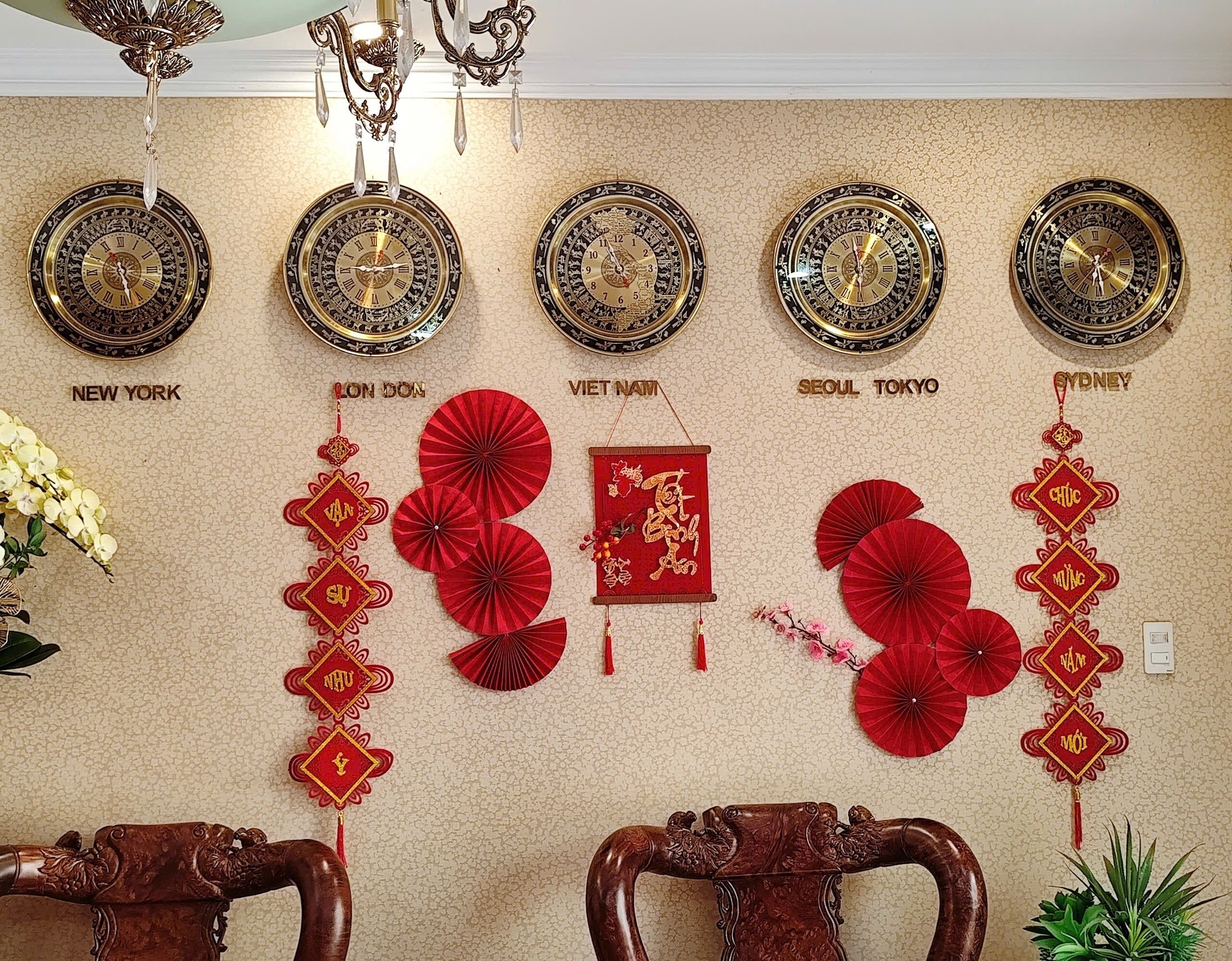 Een muur met klokken waarop stadsnamen staan, rode decoratieve waaier(s) en een rode hangende versiering met Chinese karakters.