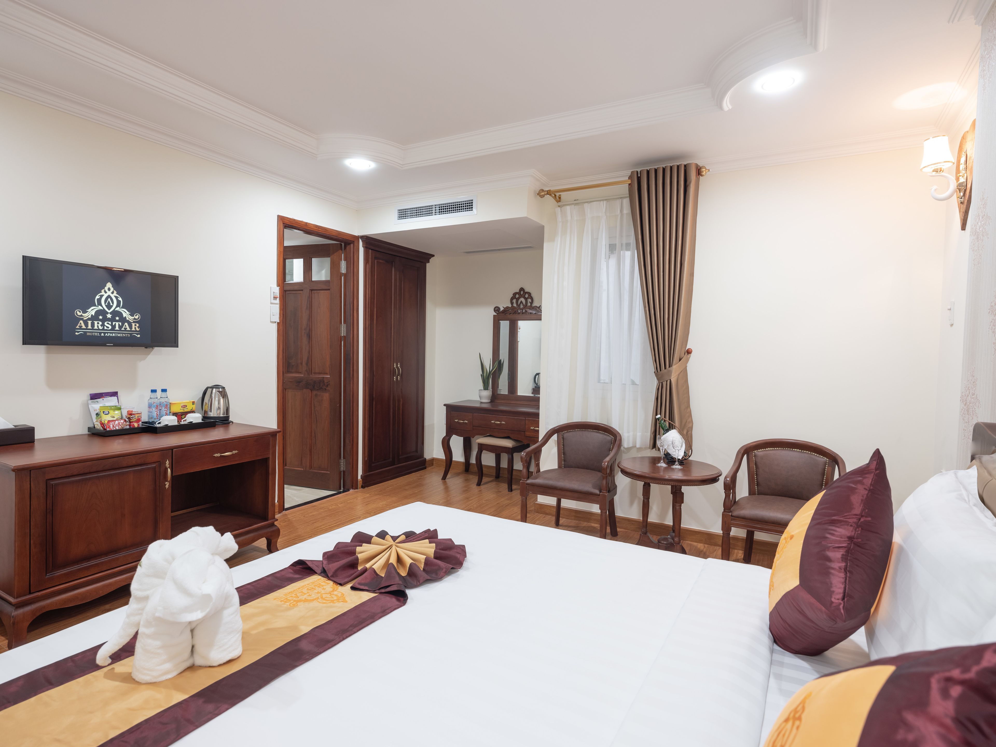 A hotel room with a bed, a desk, a chair, a small table, a television, and a wardrobe.