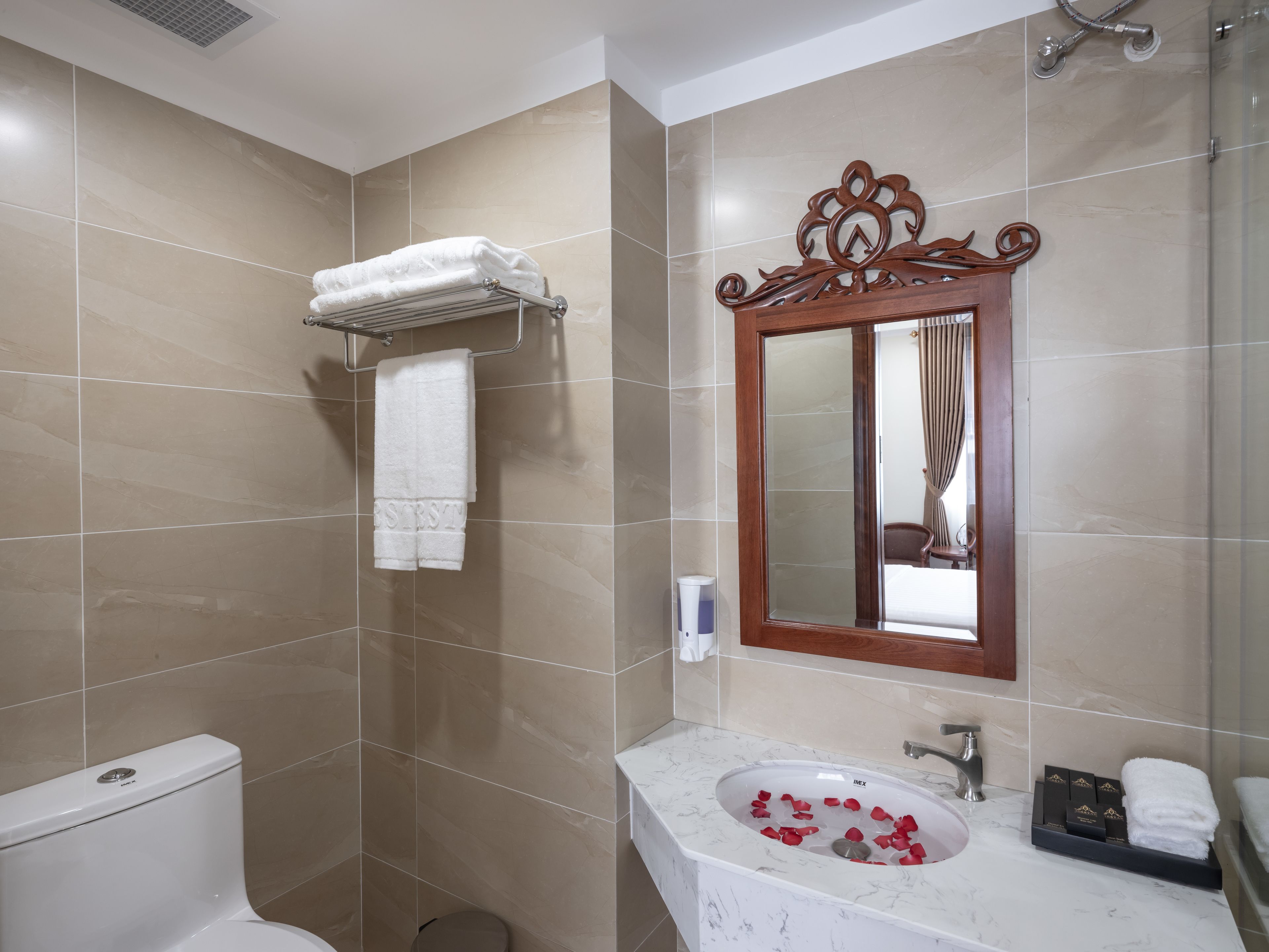 Un baño con inodoro, un lavabo decorado con pétalos de rosa, un perchero y un espejo con marco de madera.