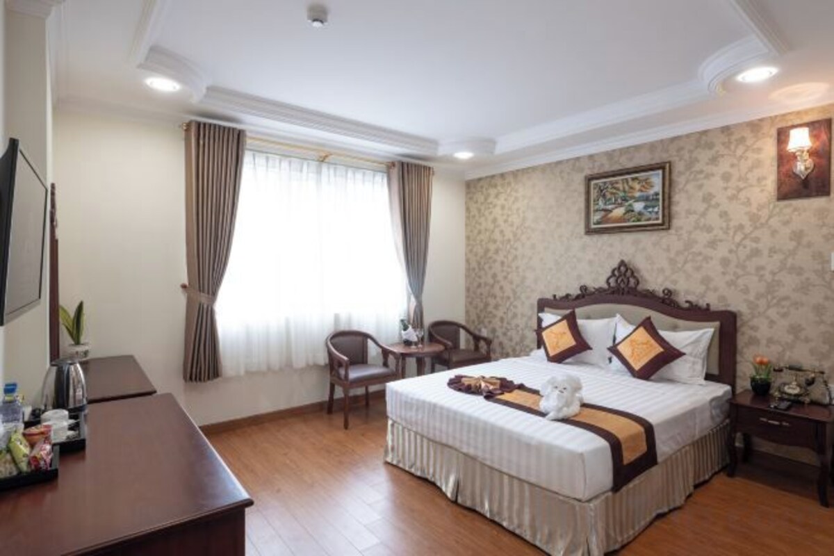Quarto de hotel com uma cama grande, escrivaninha, cadeira, televisão e janela com cortinas.