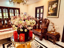 Una habitación con un arreglo floral grande sobre una mesa redonda, muebles de madera y un cuadro en la pared.