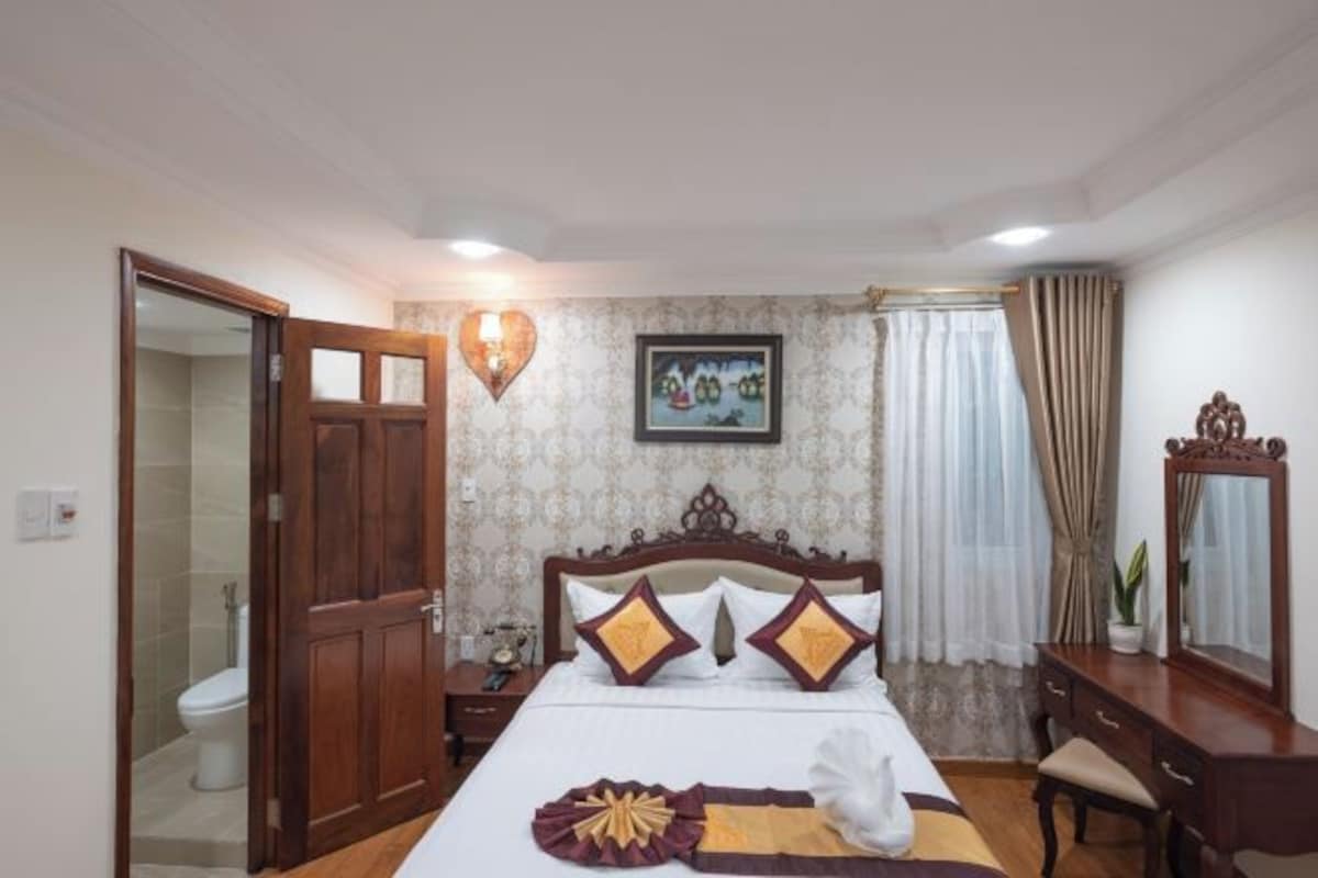 A hotel room with a wooden bed, a nightstand, a dresser, a mirror, and a bathroom visible through an open door.