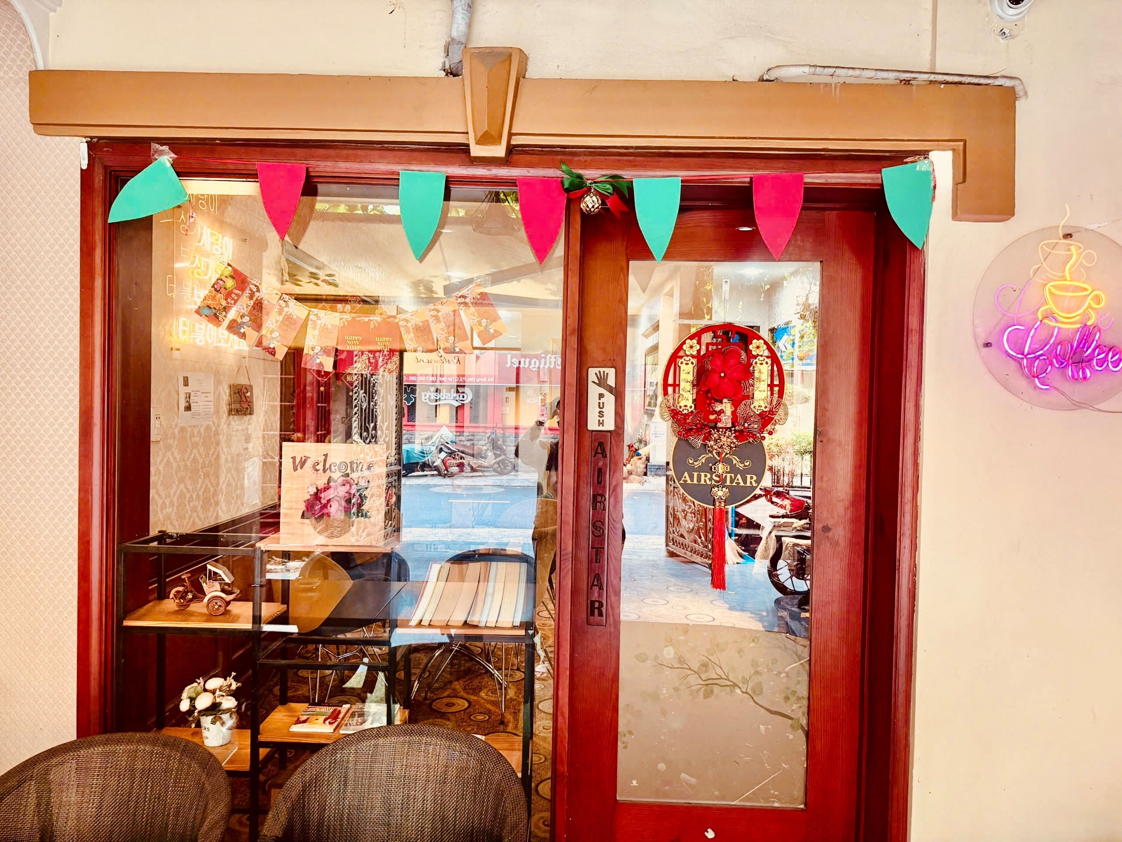 A storefront with a wooden door, a neon coffee sign, and a 'Welcome' sign.