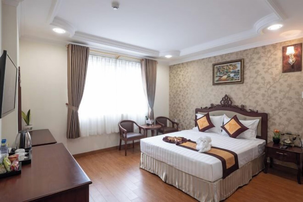 A hotel room with a large bed, a desk, a chair, a TV, and a window with curtains.