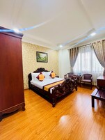 Een hotelkamer met een houten bed, een houten kledingkast, een tafeltje met stoelen en een raam met gordijnen.