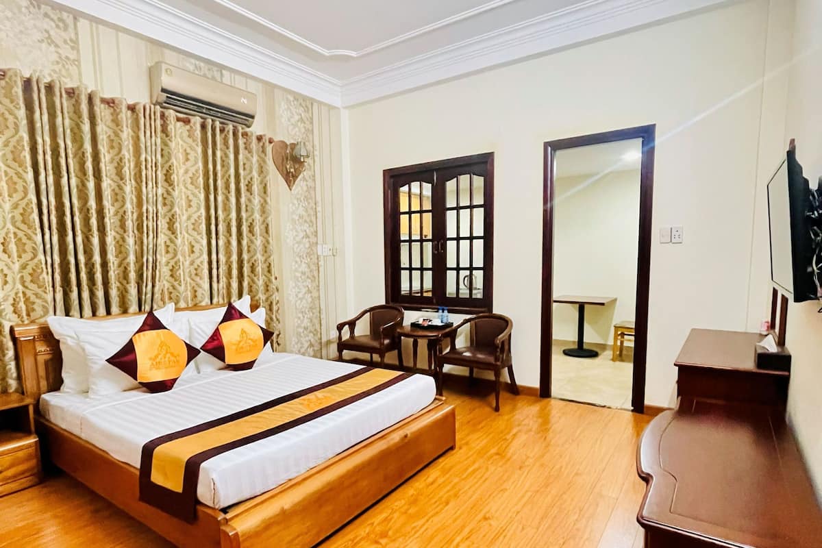 A hotel room with a wooden bed, a desk, and a chair. There is a mirror on the wall and a door leading to another room.