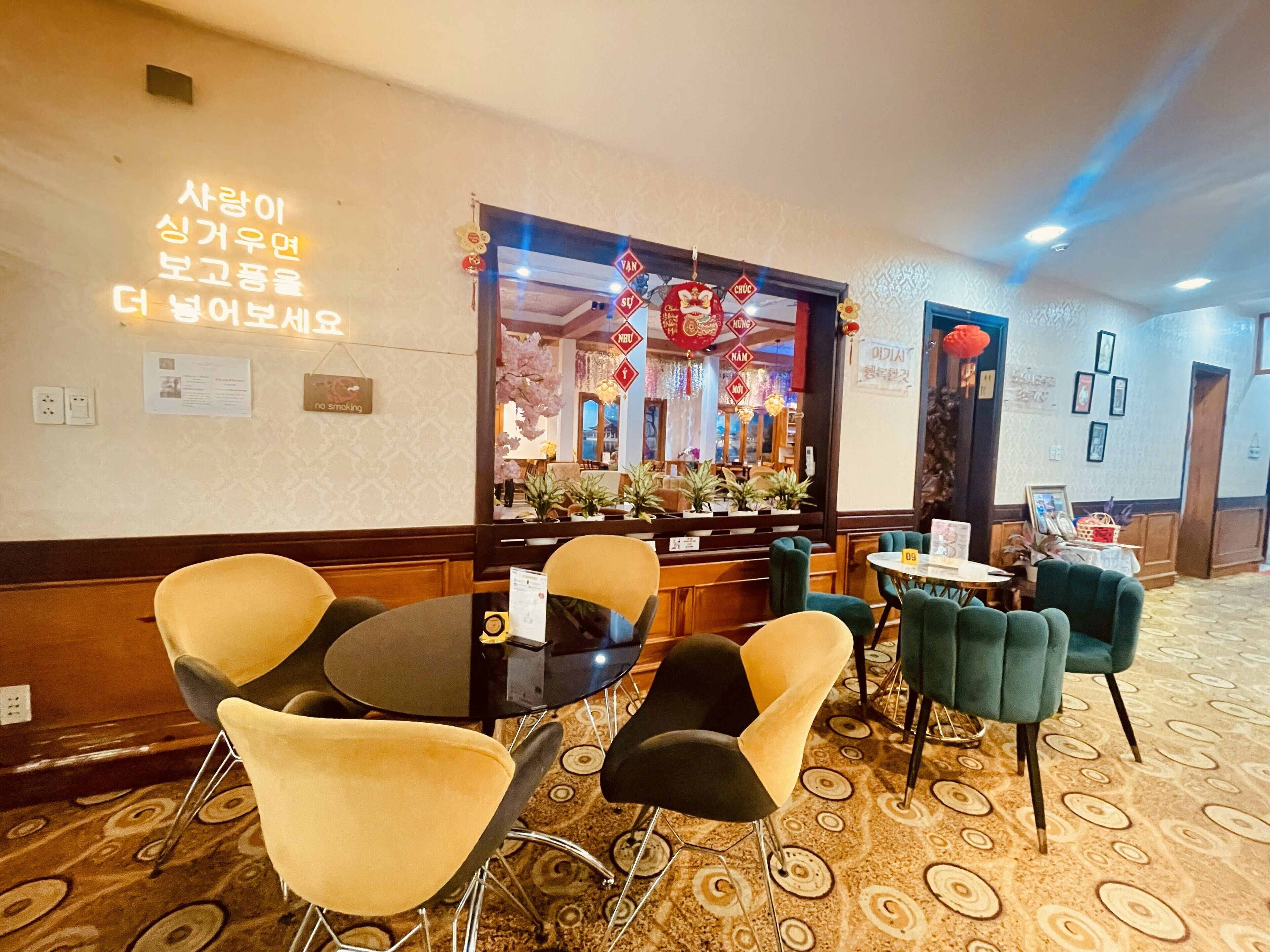 Un hall d’hôtel comprenant un comptoir d’accueil, un espace détente avec des chaises et des tables, et un tapis à motifs.
