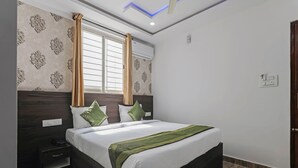 Une chambre à coucher avec un grand lit, une tête de lit en bois foncé, un papier peint à motifs, une fenêtre avec des rideaux et une table de chevet avec un téléphone.
