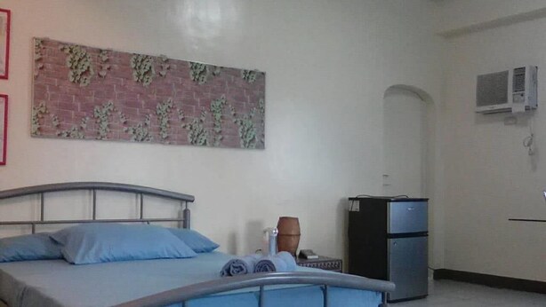 A bedroom with a bed, a small table, a chair, a refrigerator, and a wall-mounted air conditioner.