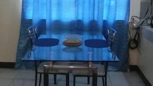 A dining area with a glass table and four chairs, a blue curtain, and a tiled floor.