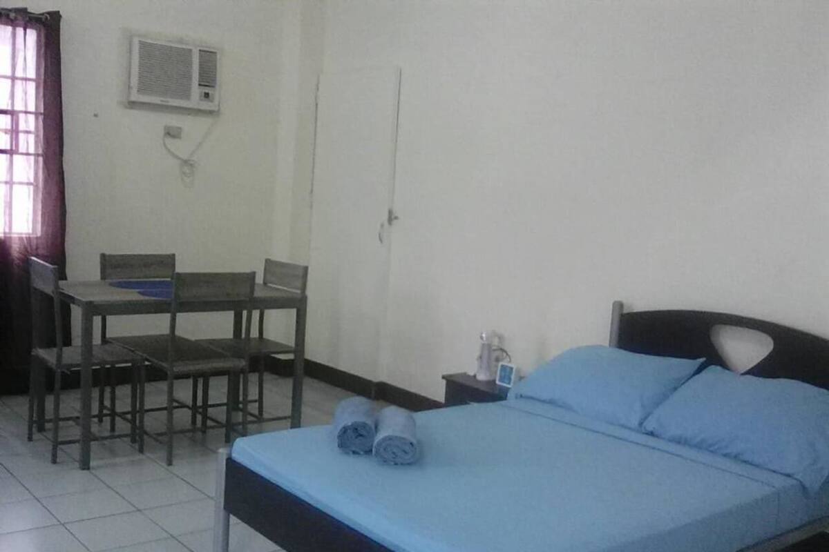 A room with a bed, a desk, and a chair. There is an air conditioning unit on the wall.