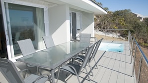 A glass-top table with chairs on a deck, a pool, and a building with large windows. - 6 Barquentine (Knysna)