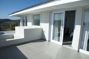 Ein modernes Gebäude mit Balkon, großen Fenstern und einer Schiebeglastür, die zu einem Innenbereich führt.