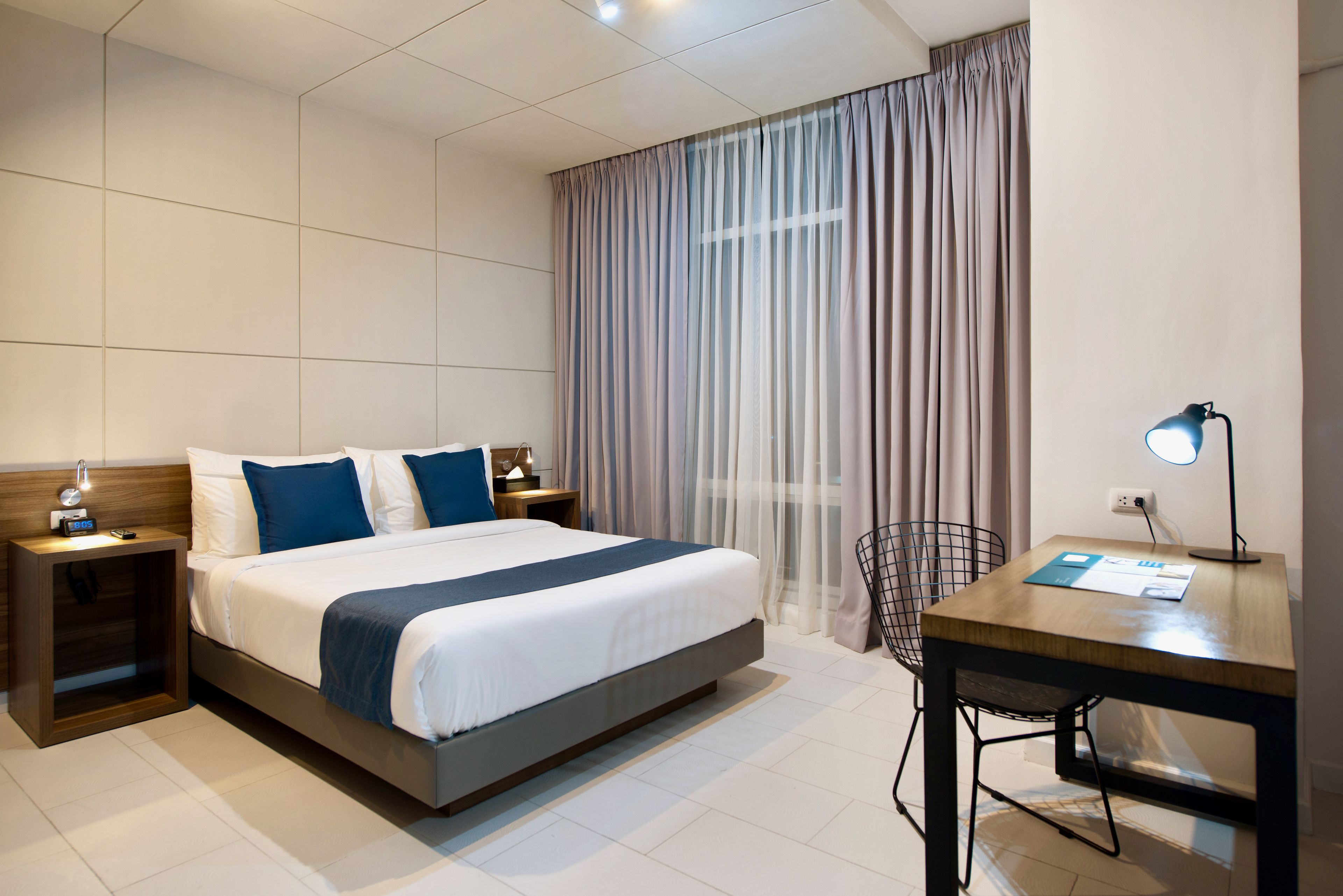 Una habitación de hotel moderna con una cama grande, mesitas de noche, un escritorio y una silla.