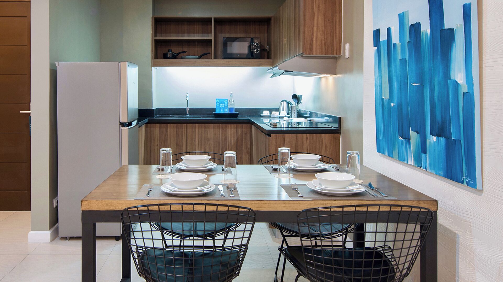 A modern kitchen with wooden cabinets, a microwave, and a dining area set for four with a table and chairs.
