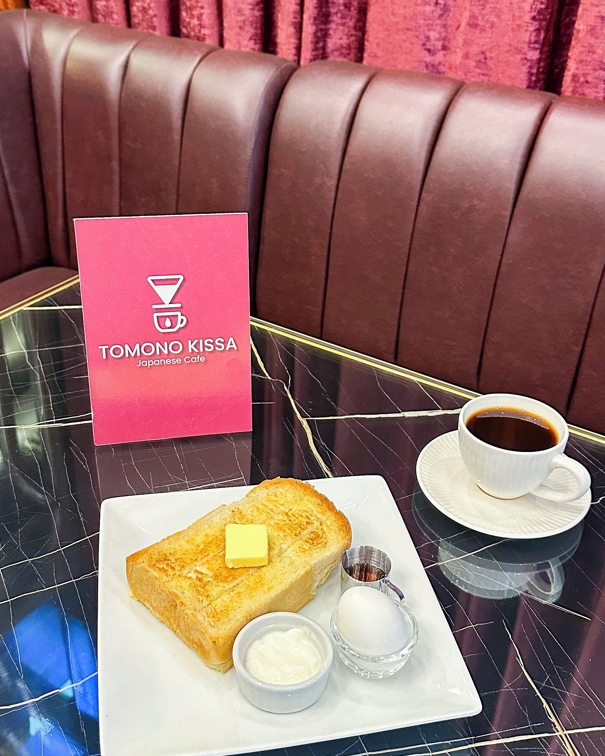 A table with a sandwich, a cup of coffee, and a menu for Tomono Kissa Japanese Cafe.