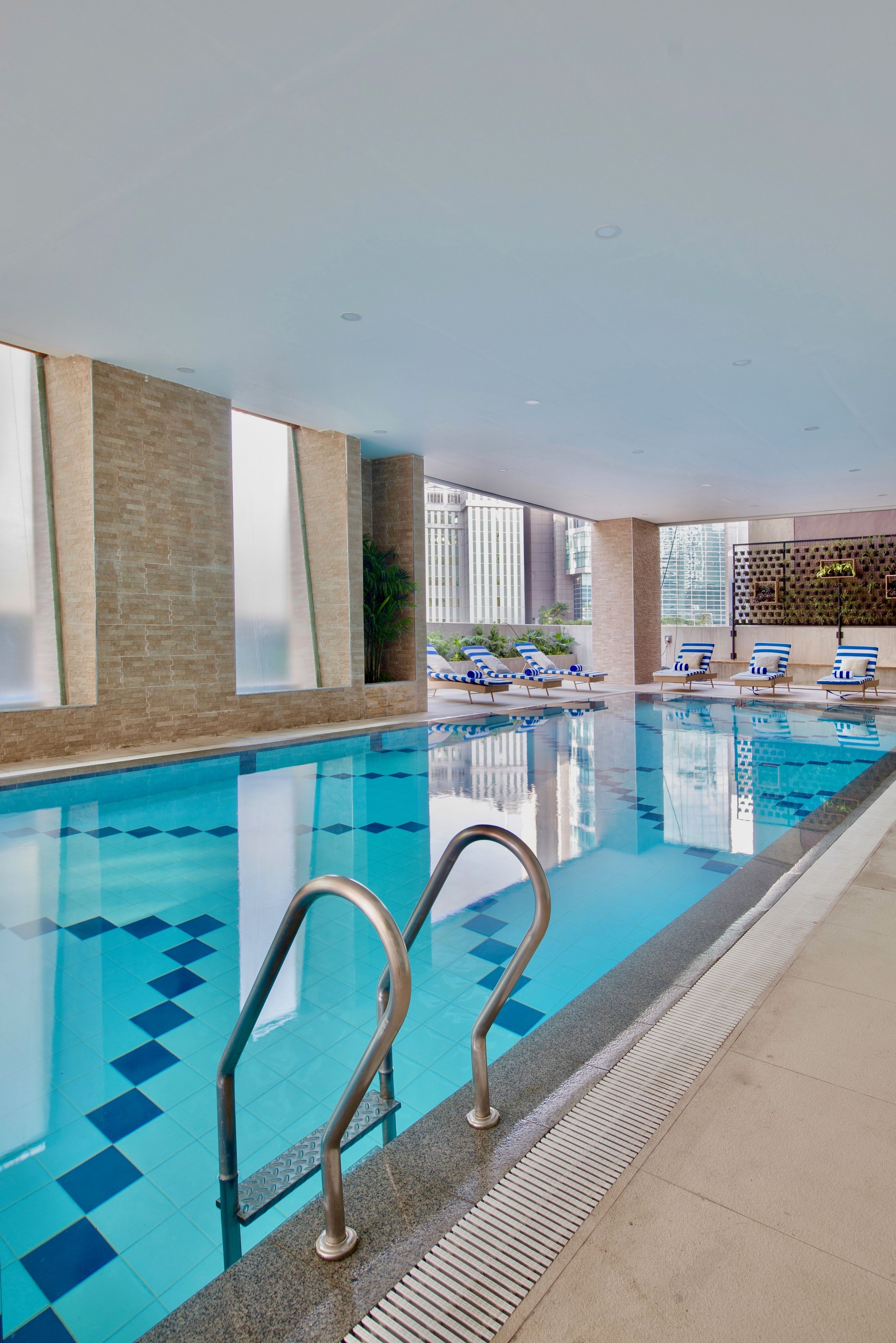 An indoor swimming pool with clear blue water, a tiled floor, and a few lounge chairs.
