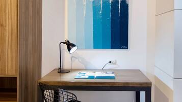 A modern workspace with a wooden desk, a black chair, a desk lamp, and a blue abstract painting on the wall.