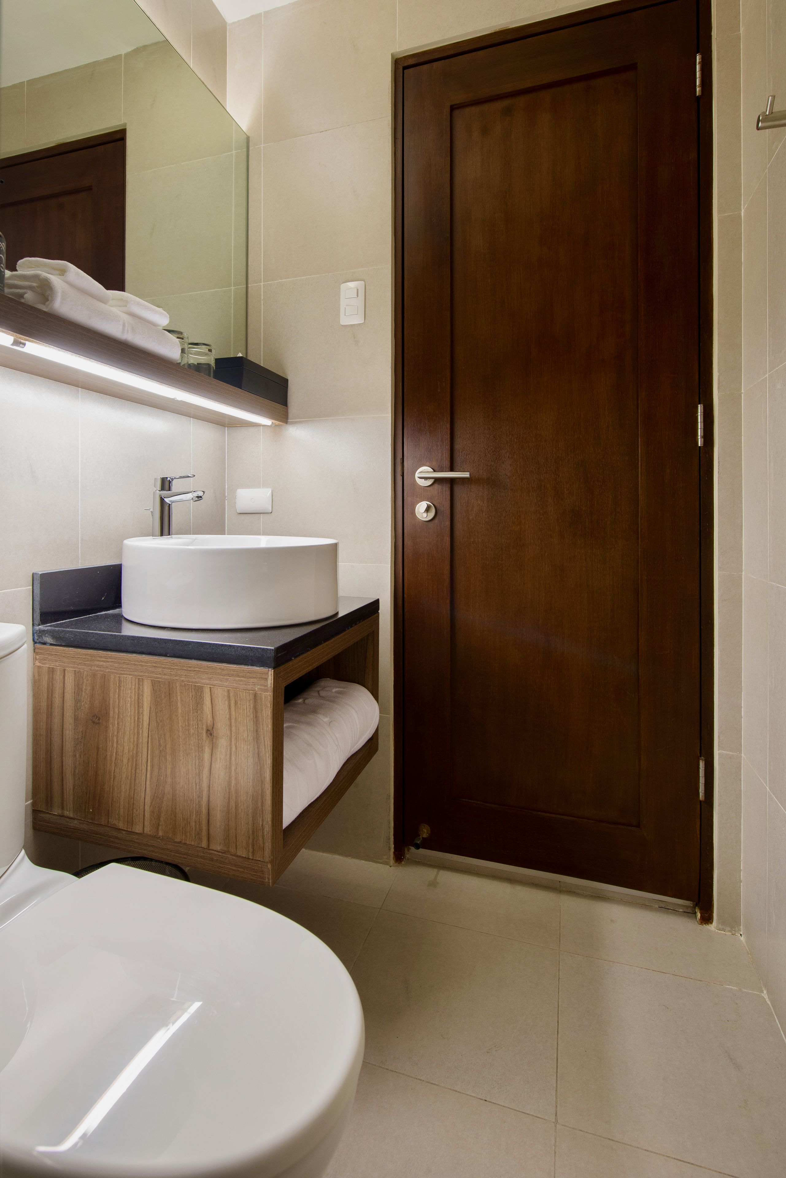 A bathroom with a wooden vanity, a white sink, and a mirror above it.