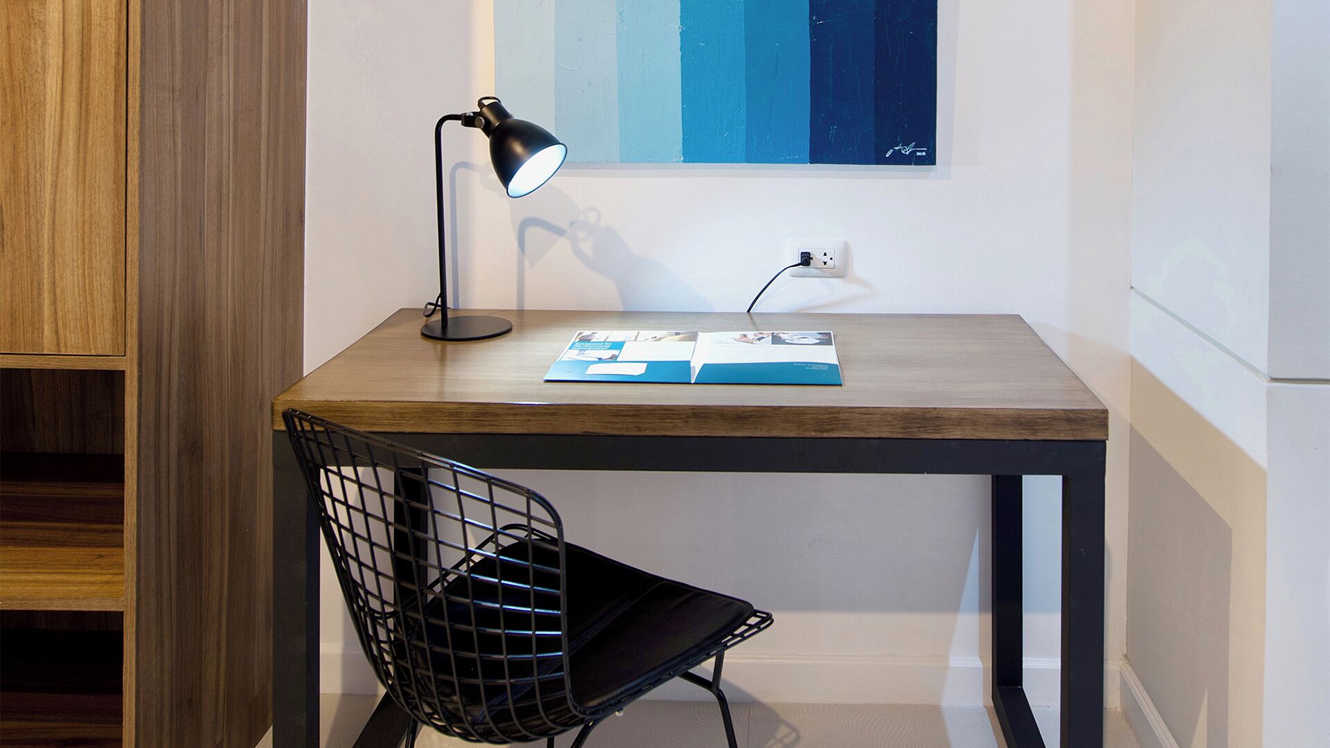 A small wooden desk with a black metal chair, a desk lamp, and a magazine on the table.