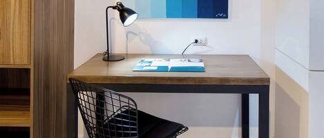 A small wooden desk with a black metal chair, a desk lamp, and a magazine on the table.