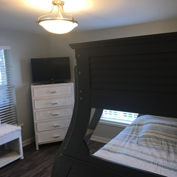 Un dormitorio con una cama de madera oscura, un tocador blanco y un televisor encima.