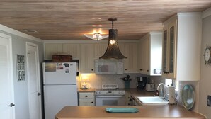 Eine Küche mit Holzbalkendecke, weißen Schränken, einer zentralen Kochinsel mit Barhocker und einer Mikrowelle.
