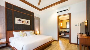 A hotel room with a large bed, wooden headboard, a wall-mounted TV, and a small table. - Villa Raeya (Krabi)