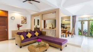 A modern living room with a sofa, coffee table, and a dining area with chairs. - Villa Raeya (Krabi)