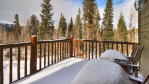 Eine Holzterrasse mit einer Bank und einem Tisch, umgeben von schneebedecktem Boden und hohen Nadelbäumen.