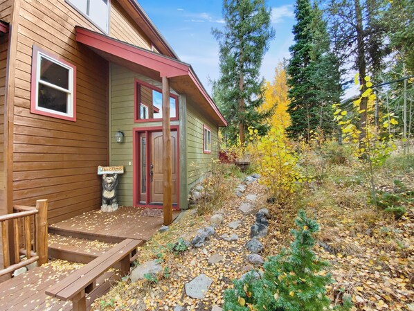 A wooden cabin with a red door, a welcome sign, and a bear sculpture.