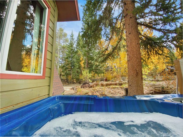 Un bain à remous situé dans un espace boisé, avec une maison en bois en arrière-plan.