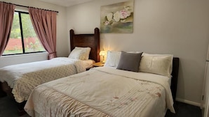 A bedroom with two single beds, a wooden headboard, a nightstand with a lamp, and a painting on the wall. - Gowrie Agapanthous - Hostel (Gowrie)