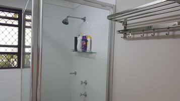 Ducha con paredes de vidrio, cabezal de ducha manual y varios grifos.
